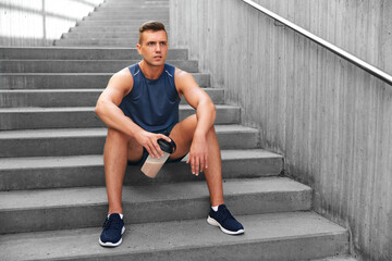 fitness, sport and people concept - tired young man with protein shake in bottle sitting on stairs