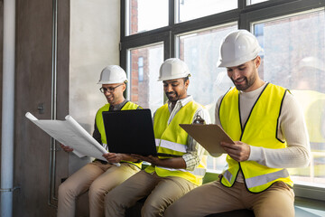 architecture, construction business and people concept - male architects in helmets with laptop, blueprint and clipboard working at office