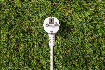 electricity, energy and power consumption concept - close up of electric plug on green grass background