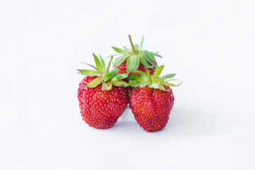 Red berry juicy strawberry. Three ripe strawberries with strawberry leaf, isolated on a white fabric background.