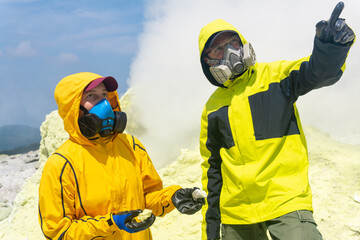 volcanologists on the slope of the volcano collect samples against the backdrop of smoking sulfur...