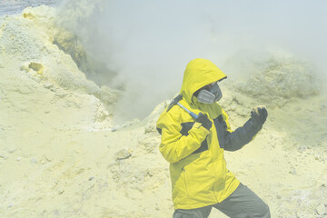 male volcanologist with a geological hammer and in a respirator on the slope of a volcano nearby...