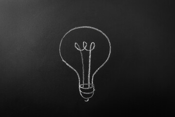 electricity, energy and power consumption concept - close up of lightbulb drawing on black chalkboard