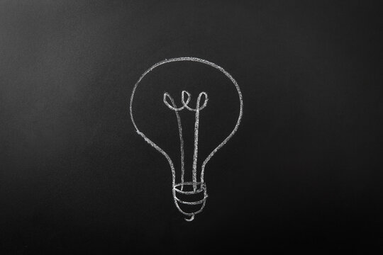electricity, energy and power consumption concept - close up of lightbulb drawing on black chalkboard