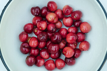 Many red cherry fruits with drops in round bowl, isolated on white closeup.