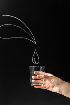drinking, environment and sustainability concept - close up of holding glass over water drop drawing on black chalkboard background