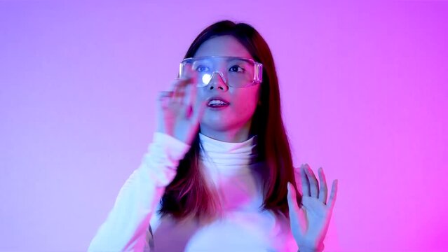 Metaverse concept, young asian woman long hair wearing clear eyeglass touching on the purple neon background. 4K video futuristic style.