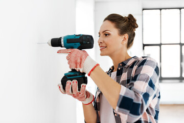 repair, construction and building concept - woman or builder with perforator drilling wall at home