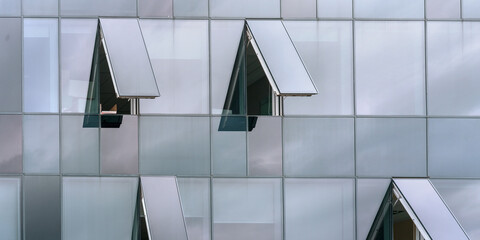 fashionable commercial office building wall of large panoramic glass windows reflects sky with grey...