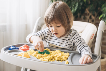 Cute little boy playing with kinetic sand. Development of fine motor skills. Early sensory...