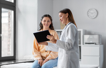 medicine, healthcare and people concept - female doctor with tablet pc computer talking to smiling woman patient at hospital - 522487262