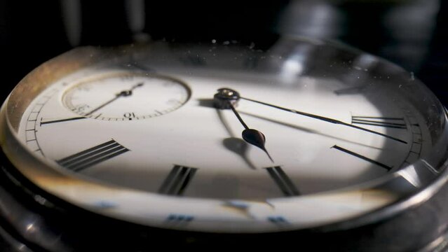 Antique pocket watch with a shadow on the dial and rotating hands in time lapse video. Old silver pocket watch with round dial and ticking hands. Running clock hands in circle in time lapse. Close up.