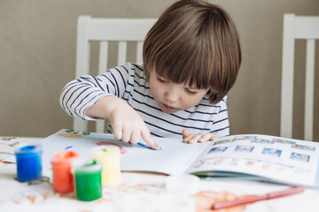 Finger painting. Portrait of cute little boy painting with fingers at home. Close-up of child's hand in colorful paints. Early education concept. Sensory play. Development of fine motor skills.