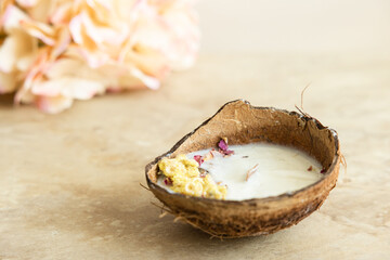 Handmade candle from soy and coconut wax in glass with wooden wick and dry flowers isolated on pastel beige background. Flat lay, top view, copy space