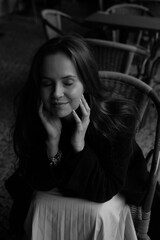 Sensual portrait of a young brunette in a white dress. Girl in a autumn wear is sitting in a chair 