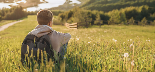 Tourist with backpack sitting on top of hill in grass field and enjoying beautiful landscape view....