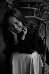 Sensual portrait of a young brunette in a white dress. Girl in a autumn wear is sitting in a chair 