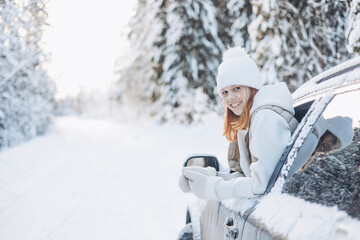 Teenager girl looking out of car window traveling in winter snowy forest. Road trip adventure and local travel concept. Happy child enjoying car ride. Christmas winter holidays and New year vacation