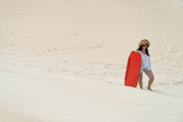Woman climbing up a sand dune with a sandboard, Kangaroo Island, South Australia - obrazy, fototapety, plakaty