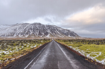 A moss-covered landscape of jumbled lava borders this narrow road in Iceland. The road continues on...
