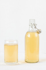 Homemade kombucha fermented drink in glass and bottle on white background. Heathy probiotic beverage with bubbles. Summer non alcoholic drinks. Copy space