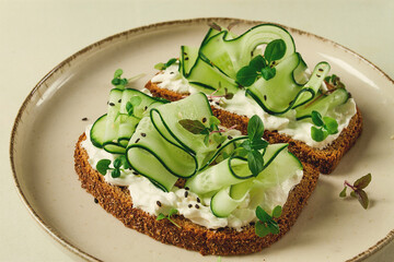 Breakfast, cereal bread sandwiches, cream cheese, sliced cucumber, with micro greenery on a light table, close-up, top view, selective focus, no people,