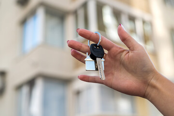 Young female realtor smiling confidently holding the key to the new house near the new house.