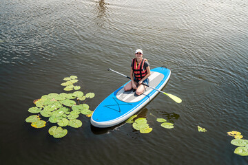 young slim woman is riding a SUP board on the city lake