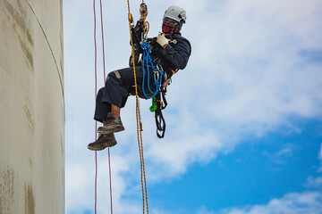 Male worker inspection wearing safety first harness rope safety line working at a high place on tank roof spherical gas  blue sky