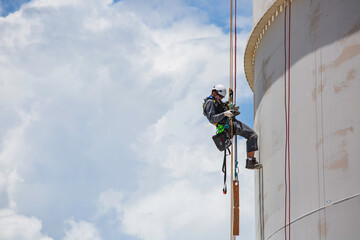 Obraz premium Male worker inspection wearing safety first harness rope safety line working at a high place on tank roof spherical gas blue sky