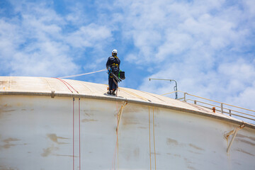 Male worker inspection wearing safety first harness rope safety line working at a high place on tank roof spherical gas  blue sky