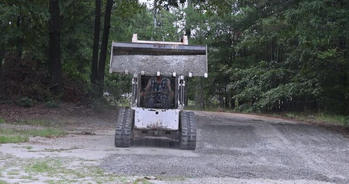 During the reconstruction of an old road, a transports Bobcat tractor is moving and unloading gravel