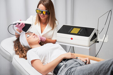 Female cosmetologist using diode laser scanner device while performing resurfacing skincare...