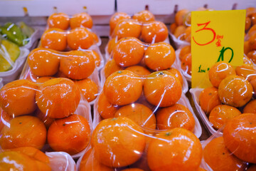 Fresh oranges at market stall display wrapped with plastic film wrap for protection of the fruits. The plastic wrappers are wasteful and unsustainable for the environment. - obrazy, fototapety, plakaty