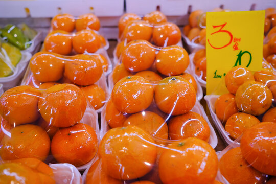 Fresh oranges at market stall display wrapped with plastic film wrap for protection of the fruits. The plastic wrappers are wasteful and unsustainable for the environment.