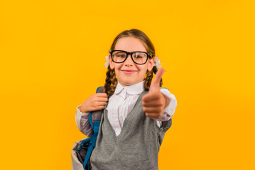 Back to school. Happy child girl gives a thumbs up on a yellow background. Education and intellectual development of children. World book day.