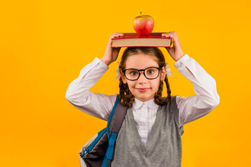 Back to school kid. Happy child holds a book and a red Apple in her head on a yellow background. Education and intellectual development of children. World book day.