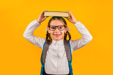 Back to school kid. Happy child holds a book in her head on a yellow background. Education and intellectual development of children. World book day.