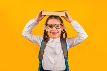 Back to school kid. Happy child holds a book in her head on a yellow background. Education and...