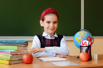 Cute schoolgirl is sitting at the blackboard in the classroom on September 1. Back to school.