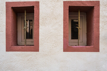 Two small windows framed in red in a white wall with roughcast