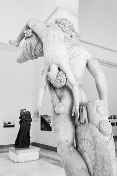Black and white photo showing ancient marble sculpture representing a strong adult man carrying on his back a young naked lad