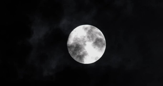 Full moon at night. The illuminated face of the moon is wrapped in a cloud cover that covers it in a veiled way.