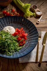 Cut cherry tomatoes, arugula and mozzarella cheese served on black plate