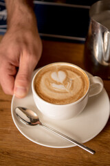 Closeup of man serving cup of cappuccino on wooden table
