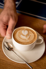 Closeup of man serving cup of cappuccino on wooden table