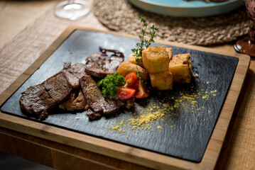 Sliced beef tongue with potatoes and tomatoes on black stone board