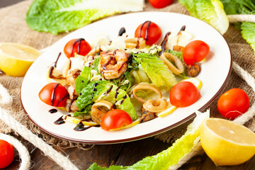 Salad with seafood and tomatoes in a plate. On a wooden table.