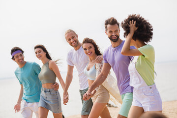 Portrait of cheerful excited fellows hug hold hands walk sand beach chatting have good mood chilling outside