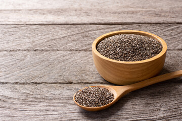 Chia seeds (Salvia hispanica) in wooden bowl and spoon isolated on wooden table background with copy space. 